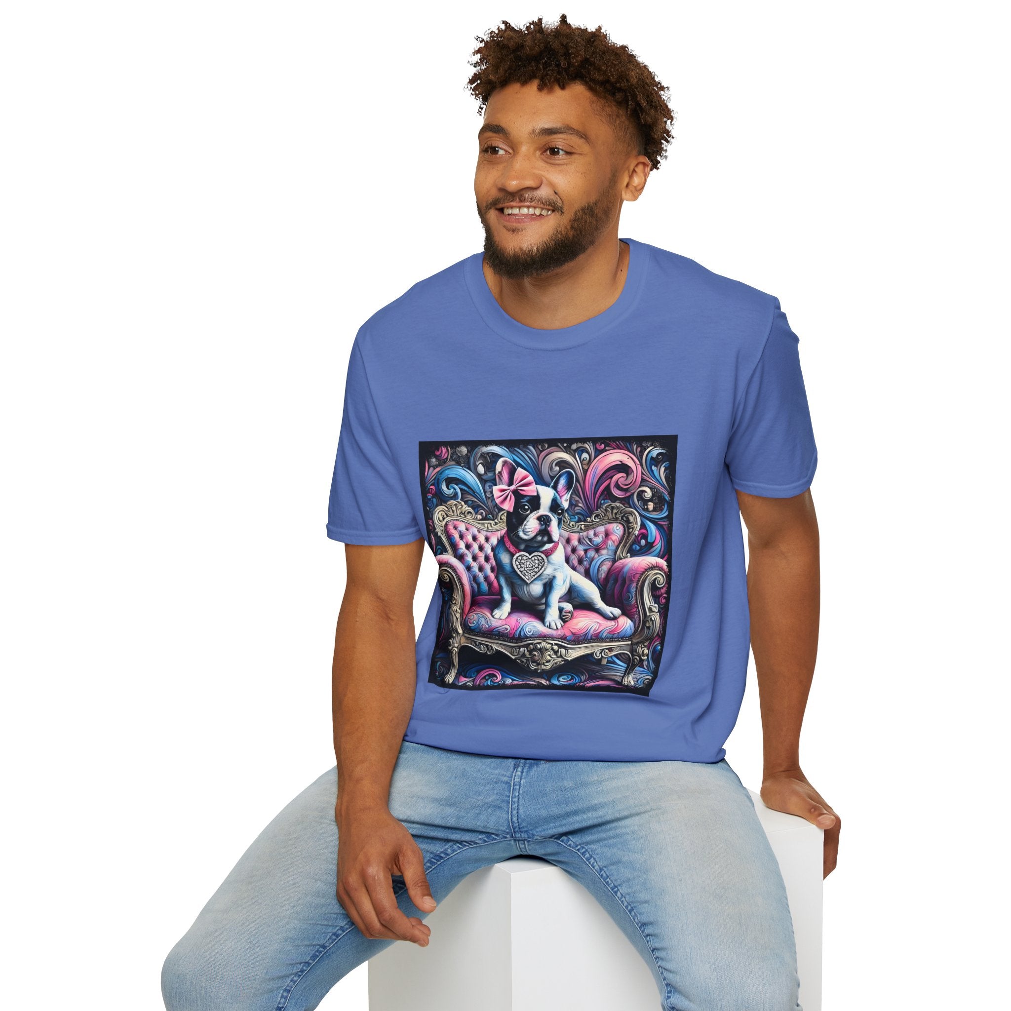 Male model in cornflower blue dog t-shirt featuring a black and white French Bulldog with a pink bow, seated on a tufted pink and gold settee against a swirling blue, pink, and purple expressionist-style background.
