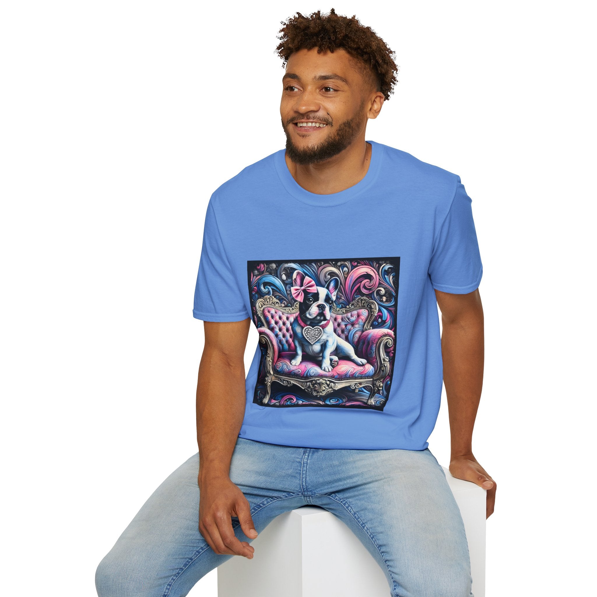 Male model in carolina blue dog t-shirt featuring a black and white French Bulldog with a pink bow, seated on a tufted pink and gold settee against a swirling blue, pink, and purple expressionist-style background.